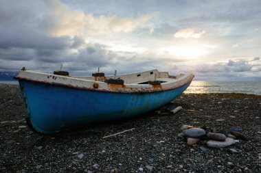 Eski terk edilmiş balıkçı teknesi gün batımında deniz kıyısında.