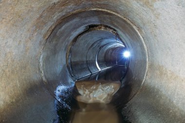 Dirty sewage flowing in round underground sewer tunnel.