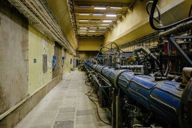Large metal tube of particle accelerator with connected pipes. Old physical laboratory building with synchrophasotron equipment clipart
