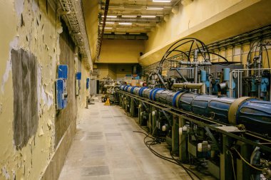 Büyük metal parçacık hızlandırıcı tüpü ve bağlı borular. Synchrophasotron ekipmanlı eski bir laboratuvar binası.