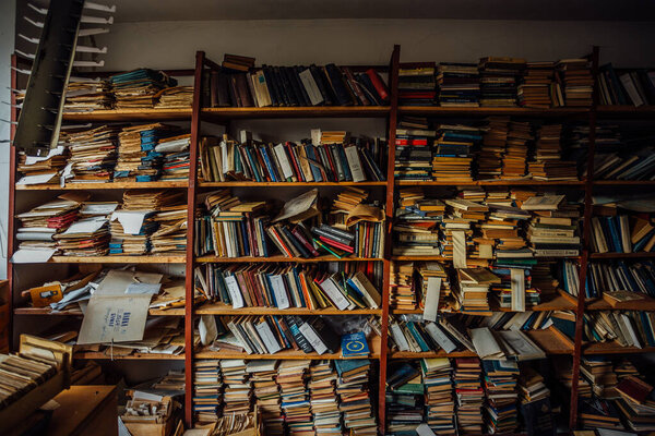 Old books on shelves in cabinet of abandoned library.