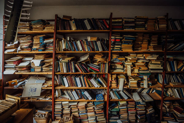 Old books on shelves in cabinet of abandoned library.