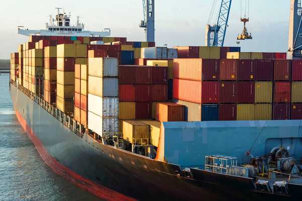 Грузовое контейнерное судно, перевозящее контейнеры под большим краном.