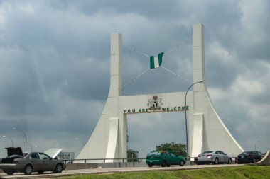 Huge metallic gate-sign holding Nigerian flag in green and white at national highway at the entrance to capitol city of Nigeria, Abuja clipart