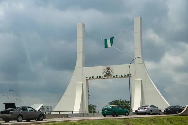 Huge metallic gate-sign holding Nigerian flag in green and white at national highway at the entrance to capitol city of Nigeria, Abuja