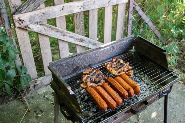 Charcoal BBQ Barbecue Grill in backyard of country side, preparing, grilling sausages and chicken on grill with wooden fence in background, the host is taking care about meat and food for family