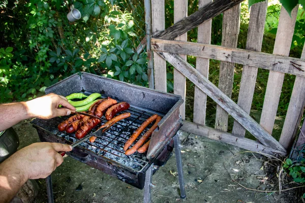 Charcoal BBQ Barbecue Grill in backyard of country side, preparing, grilling sausages and green peppers on grill with wooden fence in background, the host is taking care about meat and food for family