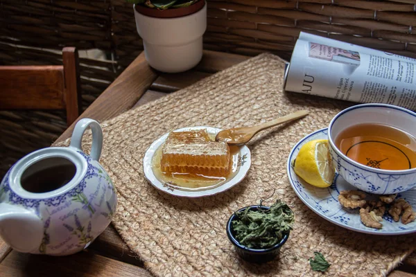 Morning setup on wooden table at balcony, books to read, cup of natural tea, teapot, organic honey from farm, fresh green tea leaves and organic fruits, in background nice view on small park between buildings in city, small oasis for relaxation