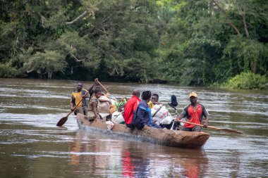 İnsanları Mbari Nehri 'nden yerel kanolarla ve feribotla geçirmek. Hafta sonu yerel pazardan satın alınan çeşitli ürünlerin rengarenk giysileri ve nakliyesi