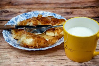 Sırp yemeği Burek (peynir turtası), kahvaltıda sofrada çatal bıçak takımı ve sarı fincanda taze yoğurt ile servis ediliyor. Sağlıklı besleyici yemek