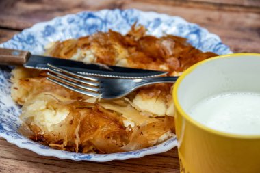 Sırp yemeği Burek (peynir turtası), kahvaltıda sofrada çatal bıçak takımı ve sarı fincanda taze yoğurt ile servis ediliyor. Sağlıklı besleyici yemek