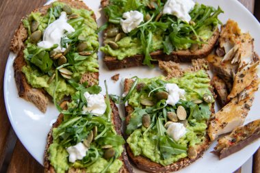 Labneh, Lemon, Maydanoz, Cheese, Edamame ve farklı kurutulmuş tohumlar, ayçiçeği ve balkabağı ile ezilmiş avokado, organik malzemelerle yapılan sağlıklı ve vegan yeşili kahvaltı.