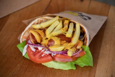 Lezzetli tortilla dürümü lezzetli bir sosis, çıtır patates kızartması, taze yeşil salata, sulu domates, lezzetli soğan ve dilimlenmiş lahana karışımıdır. Hepsi keskin hardal ve tatlı ketçapla paketlenmiştir..