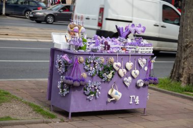 A senior lady sells lavender at a small street stand, both the stand and her jacket adorned in lavender colors, creating a vibrant, aromatic scene. clipart