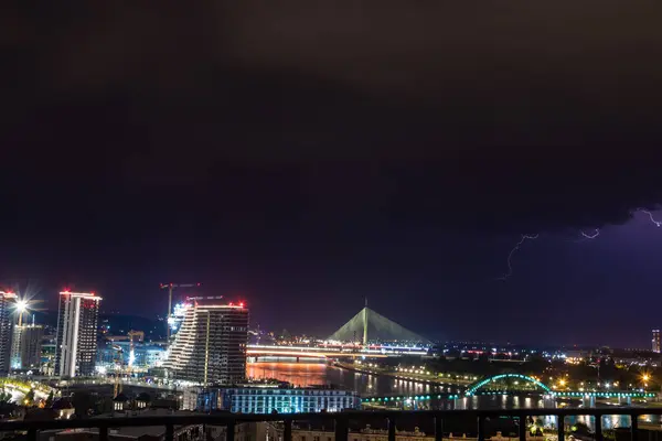 stock image A storm rages over the urban cityscape from a high viewpoint, with thunders and lightning flashes illuminating the dark sky and several bridges in the panoramic view.