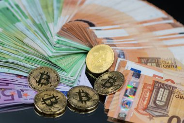 Altın Bitcoin paraları, modern finans sektöründe geleneksel ve dijital para birimi arasındaki etkileşimi sembolize eden bir yığın Euro banknotunun yanına yerleştirilmiştir.