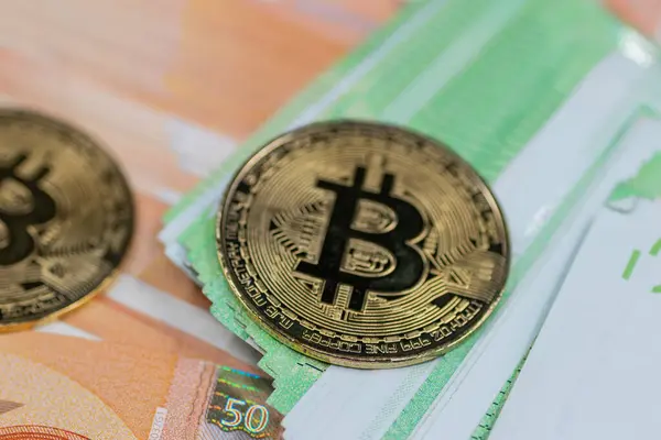 Altın Bitcoin paraları, modern finans sektöründe geleneksel ve dijital para birimi arasındaki etkileşimi sembolize eden bir yığın Euro banknotunun yanına yerleştirilmiştir.