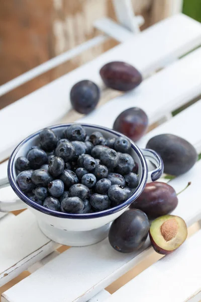 蓝莓在一个搪瓷碗和新鲜的李子里 乡村般的生活 健康的水果放在一个白色的时髦的桌子上 免版税图库图片