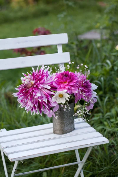 カントリーガーデンはまだ日当たりの良い夏の日にヴィンテージチェアとピンクのダリアの花で生活 ストックフォト