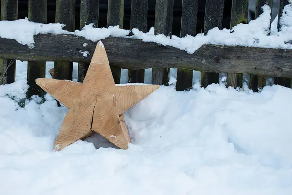 冬はまだ雪の中の田舎の木製フェンスの前に素朴な木製の星と暮らしています ロイヤリティフリーのストック写真