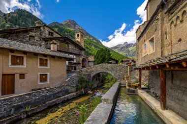 Alp deresi, Kuzey İtalya 'nın Piedmont kentindeki küçük bir köy olan Chianale' de arka plandaki dağlar gibi eski evler arasında ortaçağ taş köprüsünün altından akar..