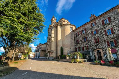 Kuzey İtalya, Piedmont 'taki Neive kasabasının eski tarihi merkezinde mavi gökyüzü altındaki parke ve katolik kilise manzarası.