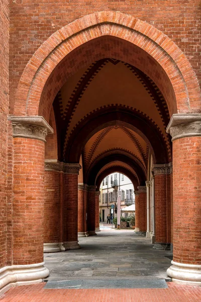 イタリア アルバの旧市街のアーチ型の天井の下の赤いレンガの壁と柱を通る通路 垂直組成 — ストック写真