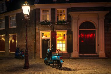 Hollanda, Amsterdam 'daki konutun önündeki kaldırım taşı caddesindeki ışıklı sokak lambasının altındaki motosikletin görüntüsü.