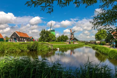 ZAANSE SCHANS, NETHERLANDS - 18 Temmuz 2007: Yeşil çimenleri yel değirmeni ve Zaanse Schans 'ın arka planında güzel gökyüzü altında evler - ünlü Hollanda köyü, popüler seyahat merkezi.