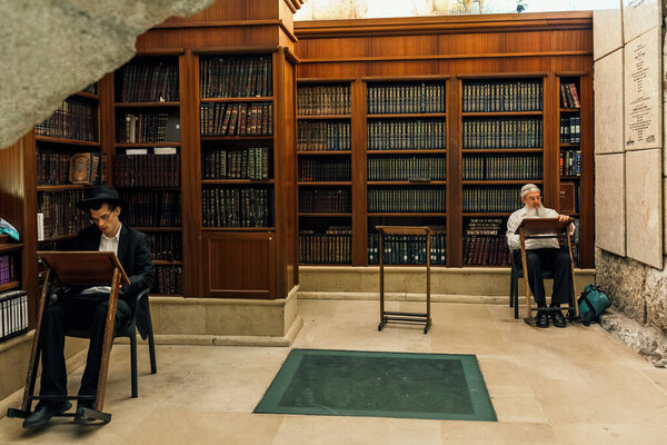 JERUSALEM, ISRAEL - JULY 04, 2016: Two religious men sit and pray among bookshelves with holy books inside of the cave synagogue  - interior part of the Wailing Wall, sacred place in judaism in Old City of Jerusalem, Israel.
