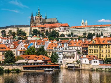 Çek Cumhuriyeti Prag 'da mavi gökyüzünün altında kırmızı çatıları ve St. Vitus Katedrali olan renkli evler.