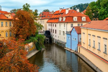 Narrow canal among colorful houses with red roofs and autumnal trees in Prague, Czech Republic. clipart