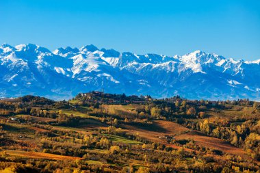 İtalya, Piedmont 'ta mavi gökyüzünün altında renkli sonbahar tepeleri ve kar dağlarının manzarası.