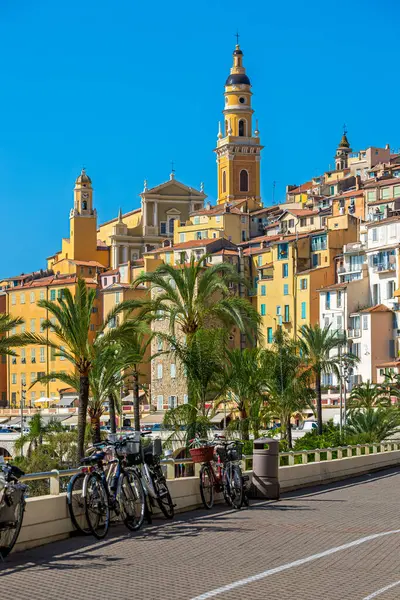 Saint Michel Archange Bazilikası, sarı cepheli ve çan kulesiyle mavi gökyüzünün altındaki eski şehir Menton, Fransa 'da renkli evler arasında.