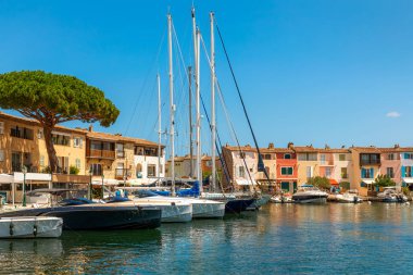 Rıhtım boyunca kenetlenmiş birkaç tekne ve yatın olduğu liman manzarası renkli evler Fransa 'nın Grimaud Limanı' ndaki açık mavi gökyüzünün altında rıhtımın hizasında..