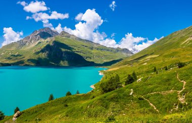 Lac du Mont Cenis 'in canlı turkuaz sularının panoramik manzarası açık mavi bulutlu Alpler' in yeşil yamaçları ve görkemli zirveleri arasında yer almaktadır..