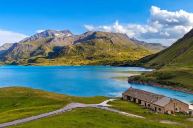 Mont Cenis Gölü 'nün turkuaz sularının panoramik bir görüntüsü. Fransa' nın Savoy bölgesinde mavi gökyüzünün altında beyaz bulutlarla çevrili Alpler..