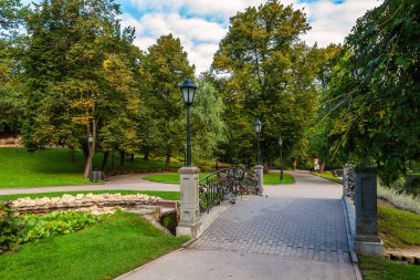 Riga, Letonya 'daki şehir parkında sokak lambaları, yeşil çimenler ve ağaçlar olan küçük köprü.