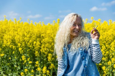 Elderly Woman smoke a cigarette in rape field with yellow blossums