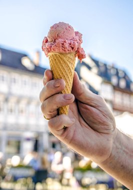 Adamın eli parlak arka planda çilekli dondurmayı tutuyor..