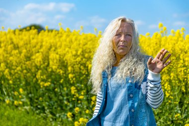 Elderly Woman smoke a cigarette in rape field with yellow blossums