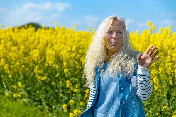 Anciana Mujer Fumar Cigarrillo Campo Violación Con Flores Amarillas Imagen de archivo