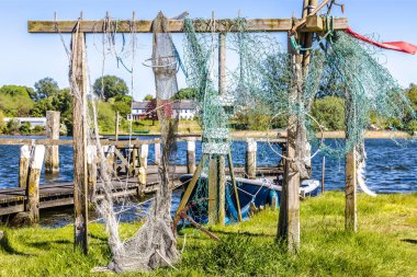 Fishing nets are drying on a wooden frame near a pier with a boat and calm water in the background. clipart