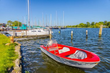 Red boat moored to a wooden pier on a calm lake, fenders hanging from a post, conveying tranquility and leisure clipart