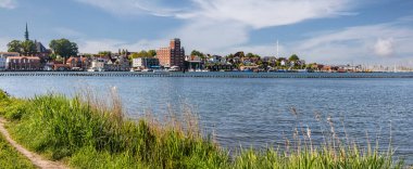 Cityscape of Kappeln, germany, with colorful buildings, church tower and harbor reflecting on the calm water of the river schlei under a blue sky clipart