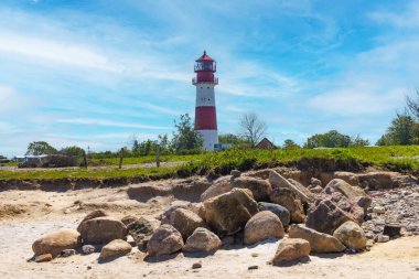 Güneşli bir günde kayalık bir sahile bakan klasik bir deniz fenerinin manzarası.
