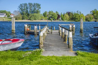 Berrak mavi gökyüzünün altında durgun göl suyuna uzanan ahşap iskele huzurlu ve davetkar bir manzara sunuyor..