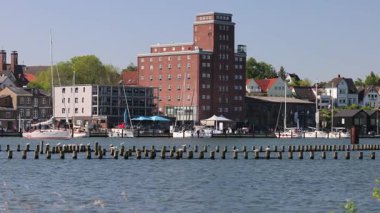 Kappeln Schlei Limanı manzaralı güneşli bir günde yelkenliler, dalgalar ve binalar. 