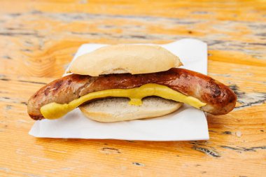 Lezzetli Alman Brtwurst sosisi, hardallı, ahşap bir yüzey üzerinde bir çöreğin içinde servis ediliyor..