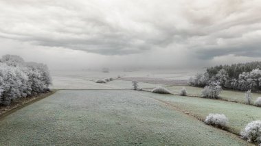 Fırtınalı bir gökyüzünün altında donuk ağaçlar ve tarlalar olan kış manzarası